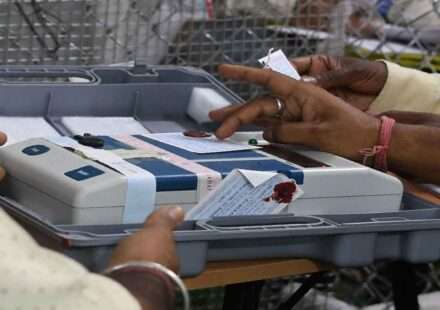 एक मतदान केंद्र पर ईवीएम मशीन की जांच करते हुए चुनाव अधिकारी, जिसमें बटन साफ और सुरक्षित दिखाई दे रहे हैं।