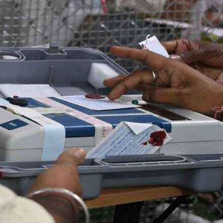 एक मतदान केंद्र पर ईवीएम मशीन की जांच करते हुए चुनाव अधिकारी, जिसमें बटन साफ और सुरक्षित दिखाई दे रहे हैं।