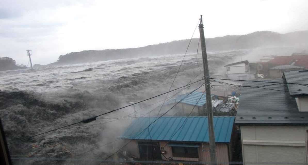 समुद्र किनारे ऊंची लहरें उठती हुई दिखाई दे रही हैं, तटीय इलाकों में चेतावनी के संकेत मौजूद हैं और लोग सुरक्षित स्थानों की ओर जा रहे हैं।
