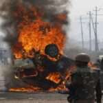 औद्योगिक क्षेत्र में प्रदर्शन कर रहे मजदूर, जलती गाड़ियां और तैनात पुलिस बल का दृश्य