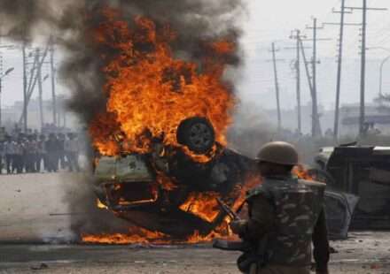 औद्योगिक क्षेत्र में प्रदर्शन कर रहे मजदूर, जलती गाड़ियां और तैनात पुलिस बल का दृश्य